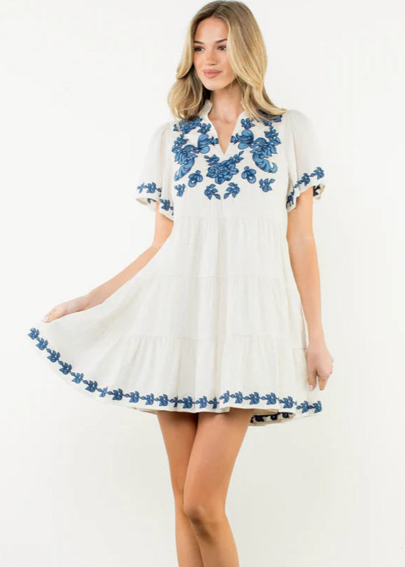 Woman wearing a white dress with blue floral embroidery on a white background