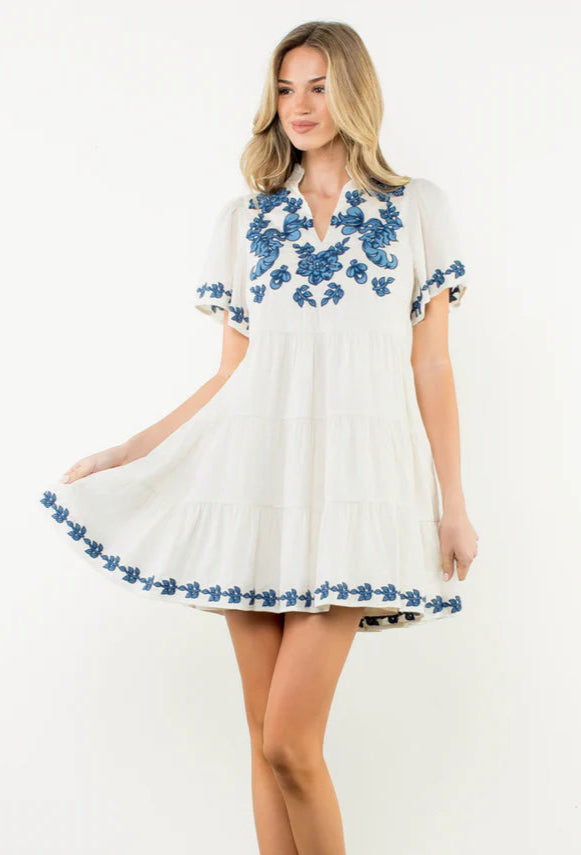 Woman wearing a white dress with blue floral embroidery on a white background