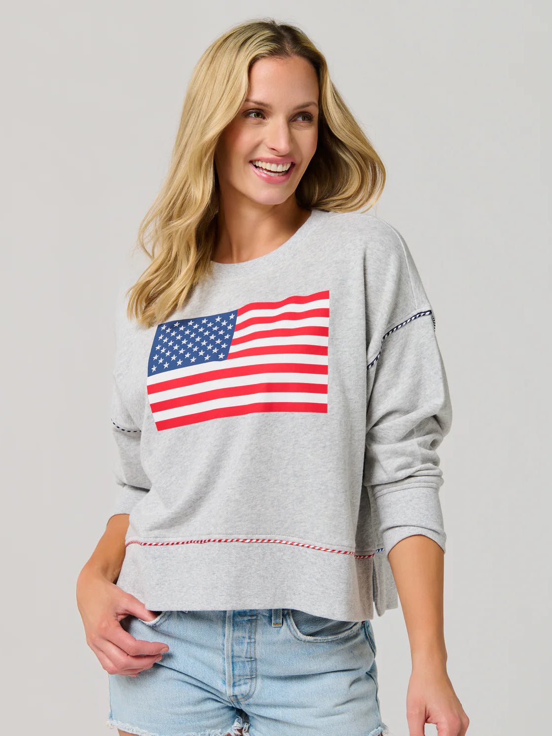 Woman wearing a gray sweatshirt with an American flag design on a plain background