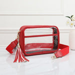A red crossbody bag with a clear front window, gold-tone hardware, a red tassel charm, and a red adjustable strap.