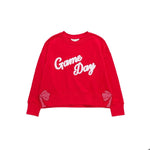 A bright red crewneck sweatshirt featuring the words 'Game Day' in white script across the chest, with Gingham bow cutout details on the lower sleeves.