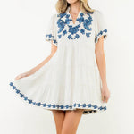 Woman wearing a white dress with blue floral embroidery on a white background