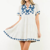 Woman wearing a white dress with blue floral embroidery on a white background