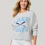 Woman wearing a gray sweatshirt with 'Lake Days' text and white shorts on a light gray background