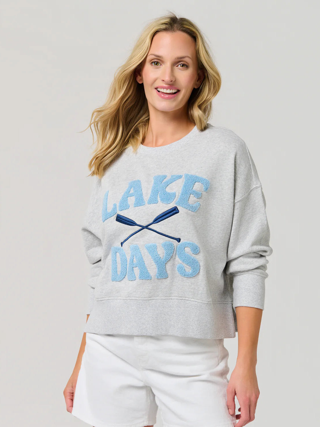 Woman wearing a gray sweatshirt with 'Lake Days' text and white shorts on a light gray background